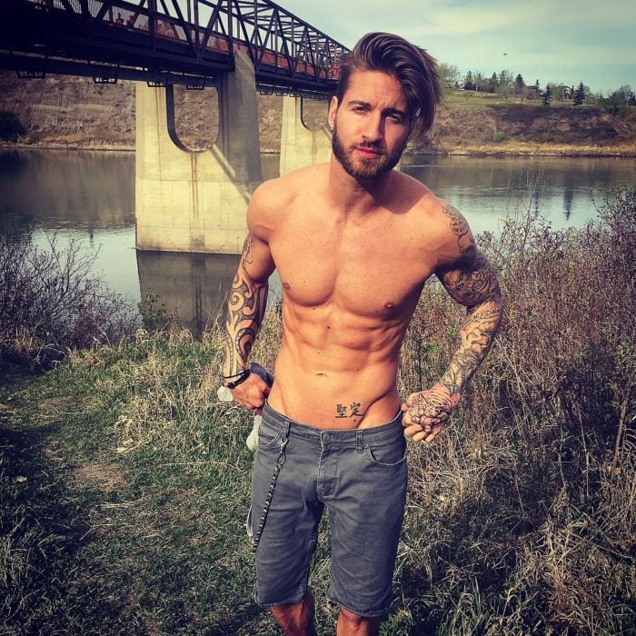 hombre sin playera y con tatuajes en lago