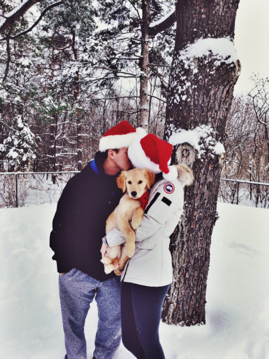 pareja con gorros de navidad cargando a perro 