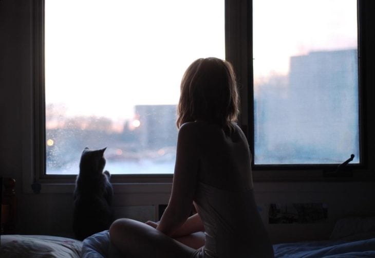 chica acompañada de su gato,, mirando por la ventana
