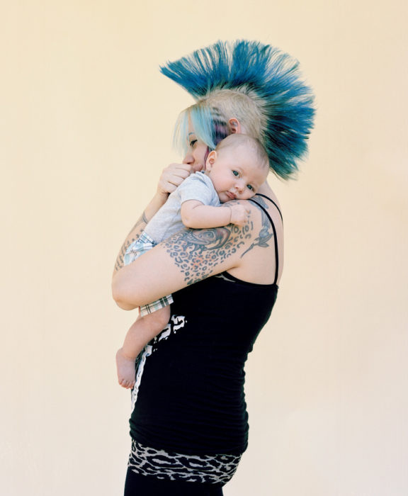 Mamá llena de tatuajes y con el cabello de colores sosteniendo a su bebé