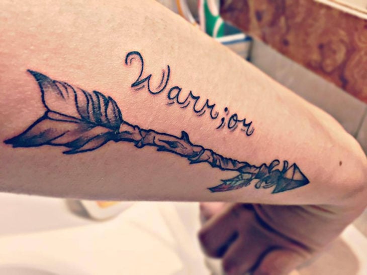 Tatuaje flecha y la palabra warrior 