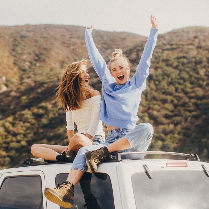 Chicas sobre una camioneta levantando los brazos y riendo 