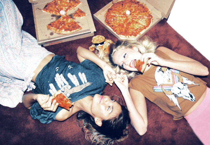 amigas acostadas comiendo pizza