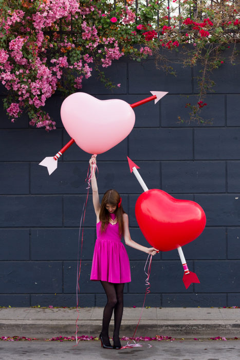 mujer con globos grandes en forma de corazones flechados