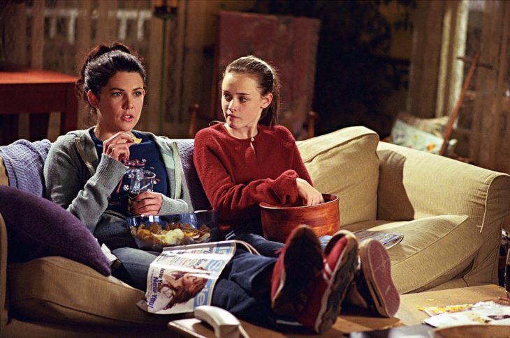 chicas viendo la televisión sentadas en sofa comiendo palomitas