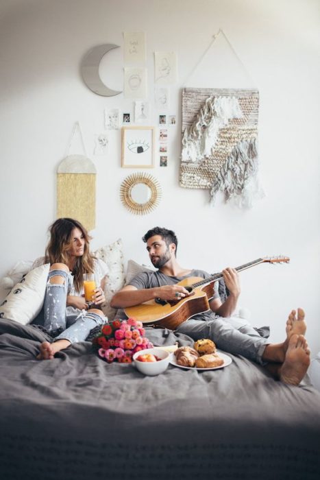 pareja relajada en cama comiendo y tocando guitarra