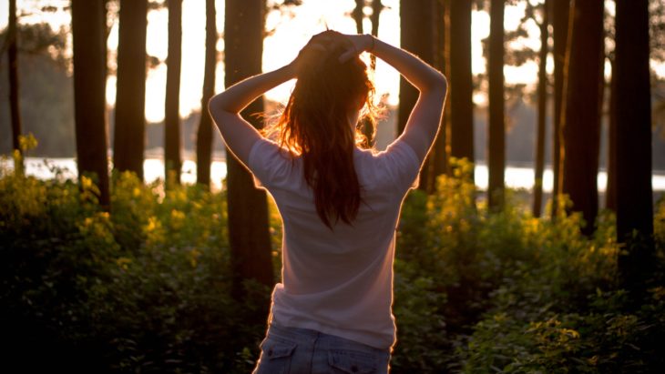 chica en el bosque con los brazos sobre la cabeza
