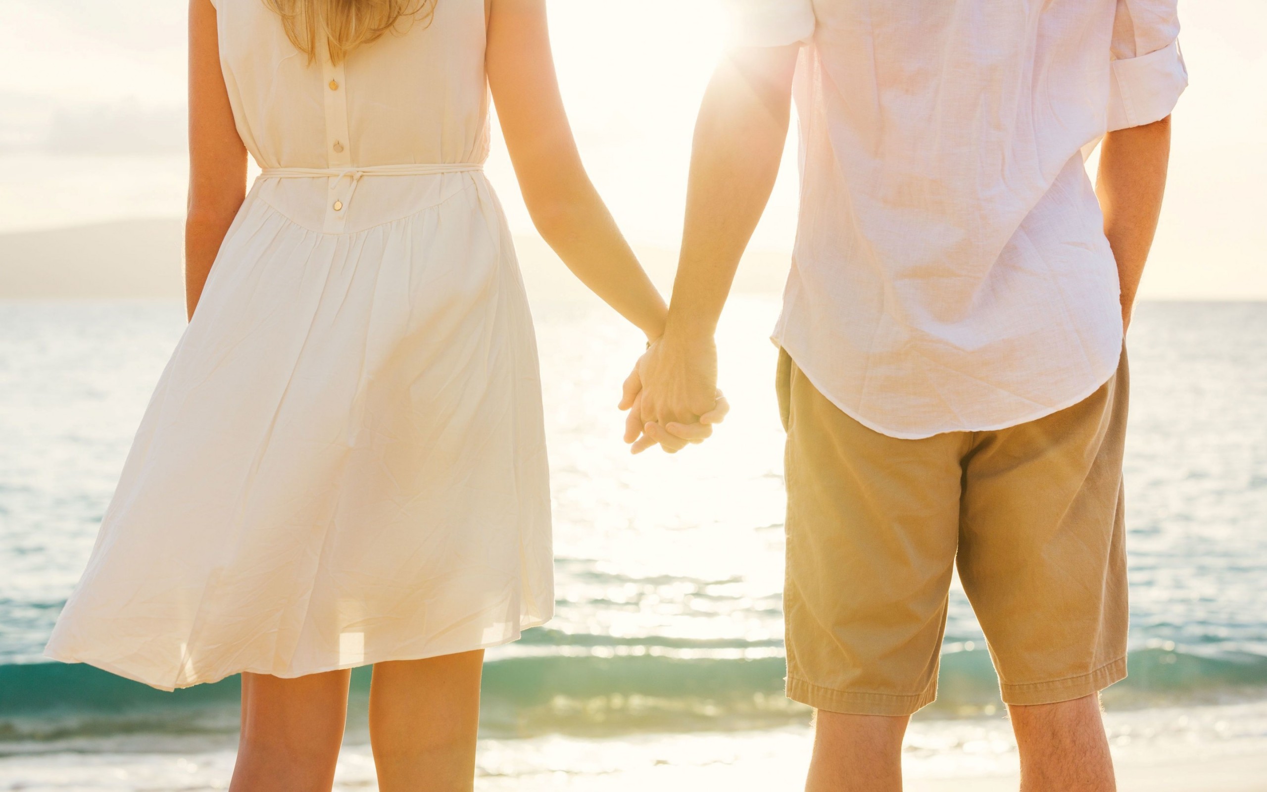 pareja tomada de la mano en la playa vestidos de blanco