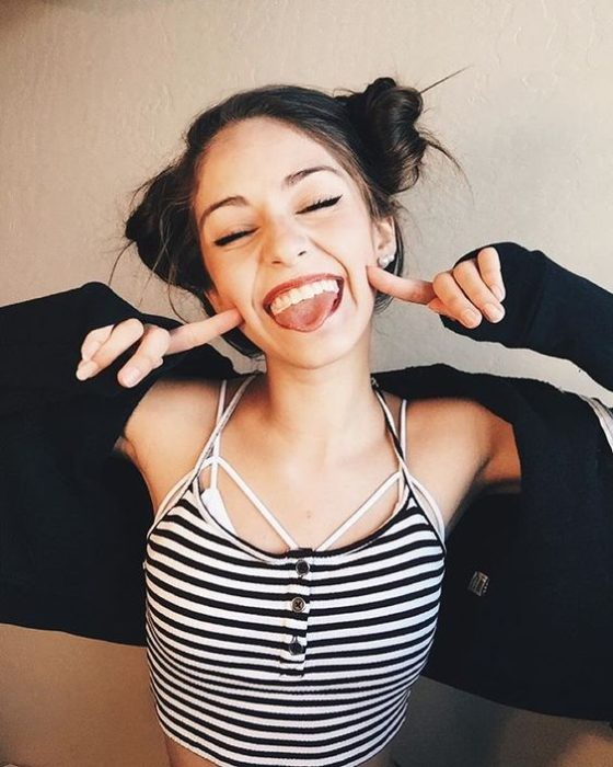 chica sacando la lengua con los dedos en las mejillas