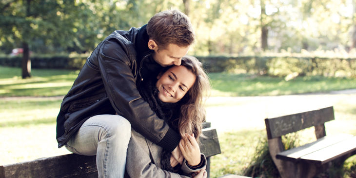 pareja beso en la frente sentados en una banca en el parque