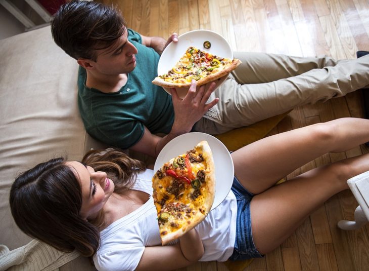pareja sentados en el piso comiendo pizza