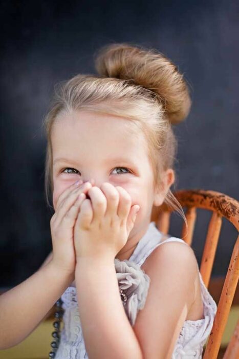 Niña sonriendo mientras cubre su boca con sus manos 