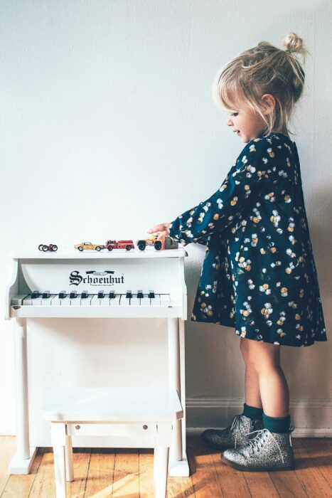 Niña jugando con sus carritos mientras están sobre un pequeño piano de juguete 