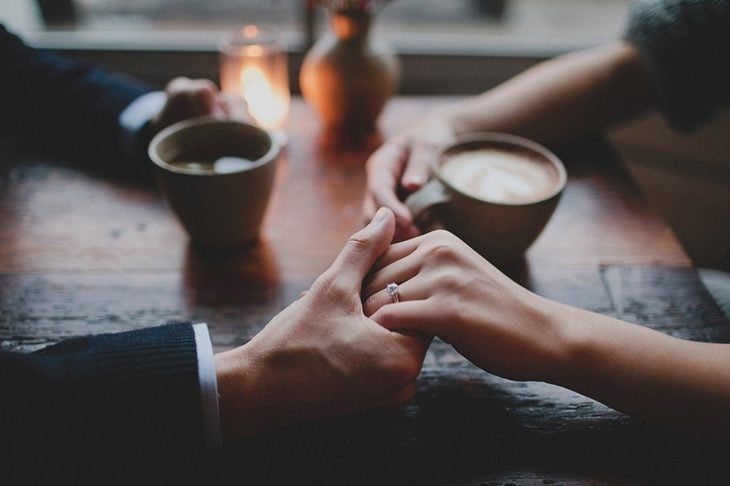 hombre sosteniendo la mano de una mujer mientras beben café 