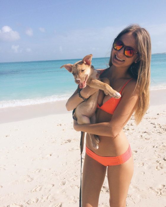 Mujer sosteniendo a un cachorro en una playa 