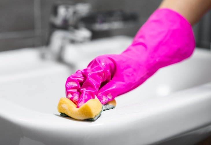 mano de mujer con guante rosa limpiando un lavabo