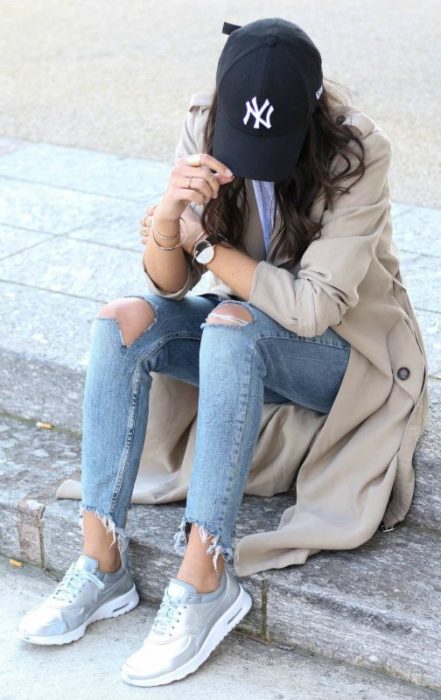 Look con gorras chica usando gorra negra con jeans y gabardina 