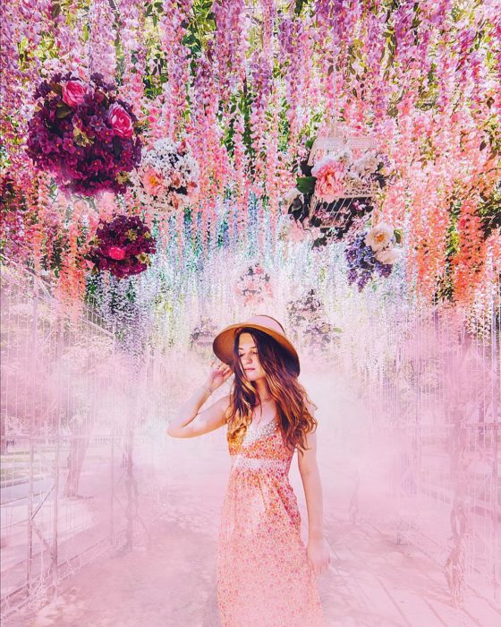 Mujer usando un vestido rosa y posando junto a flores que caen del cielo 