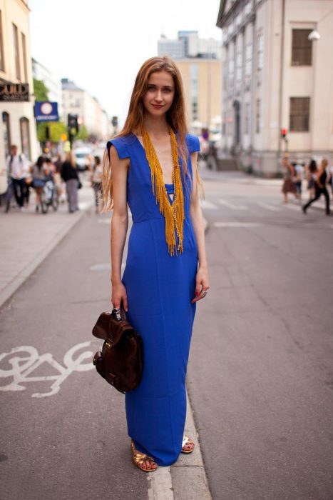 Chica usando un vestido azul y largo con un collar amarillo