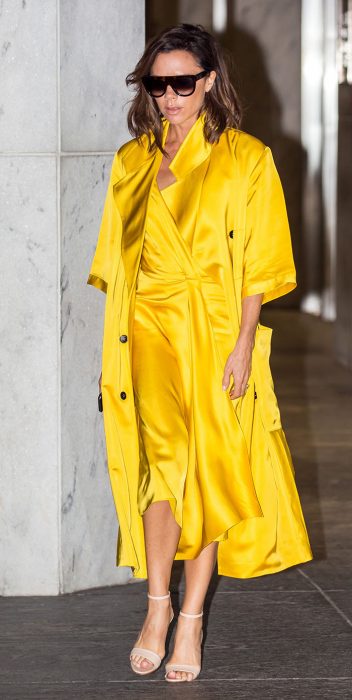 Victoria Beckham usando un vestido amarillo y un trench coat de la misma tela 