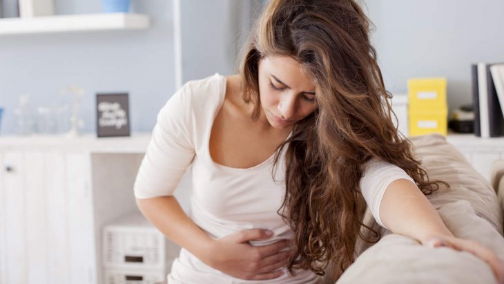 Young woman sitting on the bed with hard stomach pain