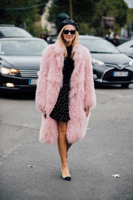 chica con falda de lunares, blusa negra y abrigo peludo rosa con boina negra