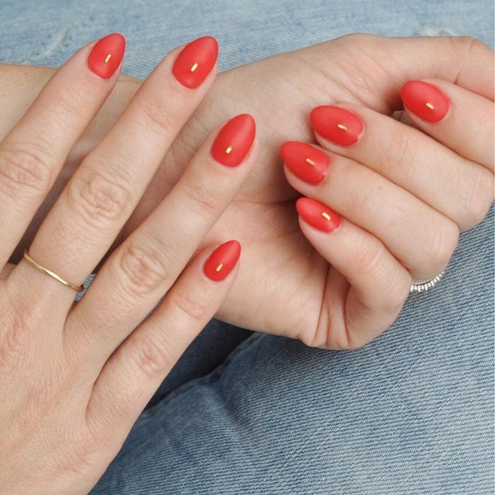 Uñas de almendra en tonos rojos con una aplicación color oro