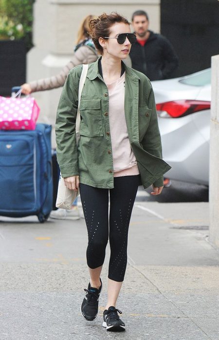 Emma Roberts caminando por la calle mientras usa una casadora verde y leggings 