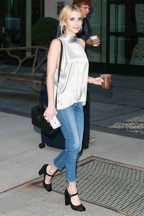 Emma Roberts caminando por la calle mientras usa una blusa de satín y jeans 