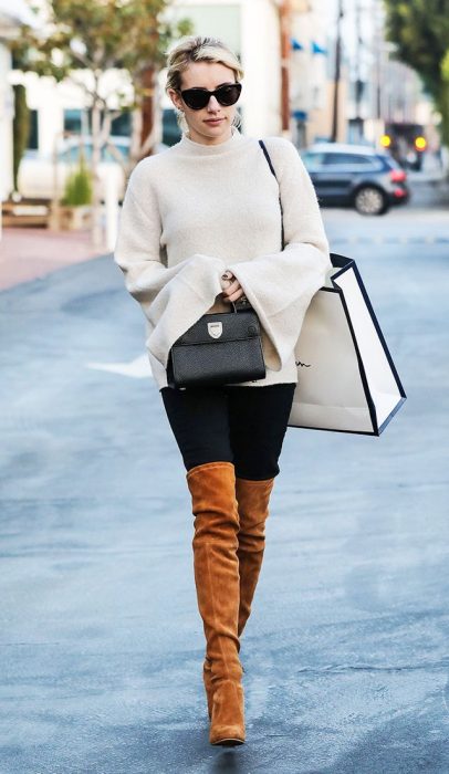 Emma Roberts caminando por la calle mientras usa un sueter largo y botas hasta el muslo 