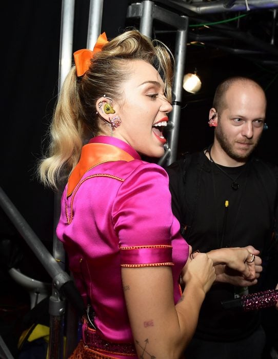 Miley Cyrus usando una coleta alta y un moño naranja 