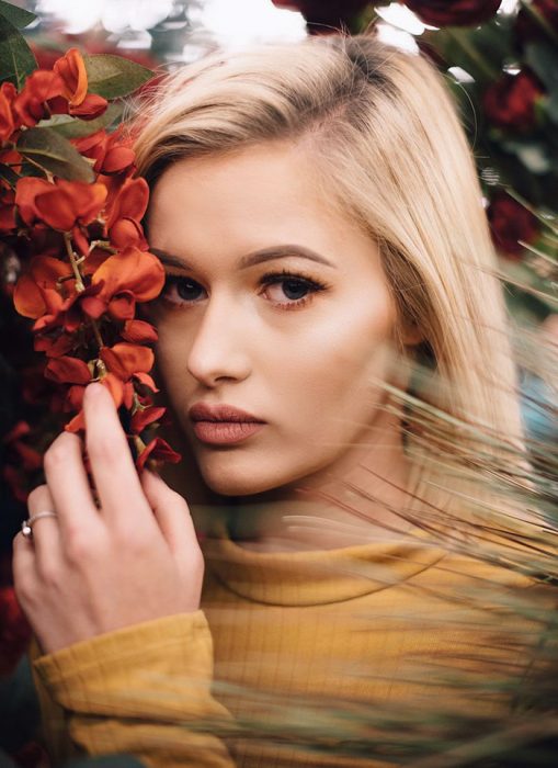 Chica recargada sobre flores sinteticas durante una sesión de fotos 