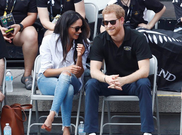 Meghan Markle usando unos zapatos flats de color café mientras está sentada junto al principe harry