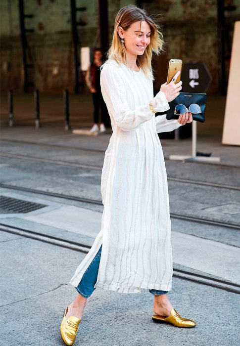 Chica usando un vestido sobre vaqueros mientras camina por la calle 