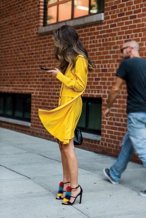 Chica usando un vestido amarillo y zapatos elegantes en color negro con aplicaciones de pompones en color azul rojo y amarillo 