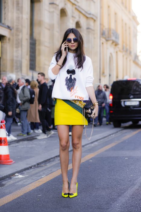 Chica usando unos zapatos amarillos con pompones junto a una falda amarilla y blusa de color blanco 