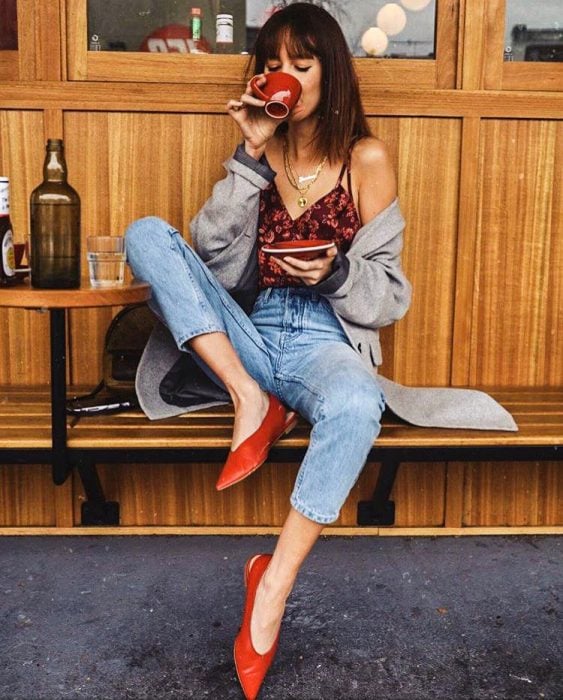 Chica sentada tomando un café mientras muestra sus zapatos de color rojo