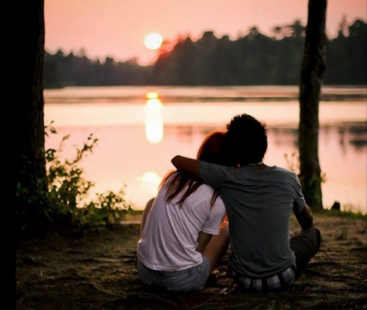 Pareja de novios abrazados besándose y viendo un atardecer 