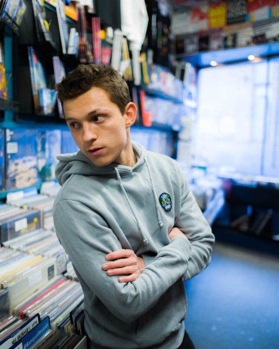 Tom Holland recargado en un estante en una tienda de discos