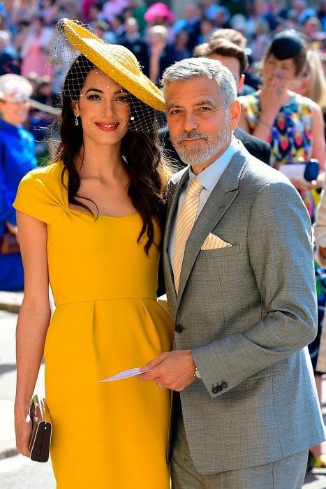 Amal Clooney usando un sombrero amarillo mientras posa junto a su esposo 