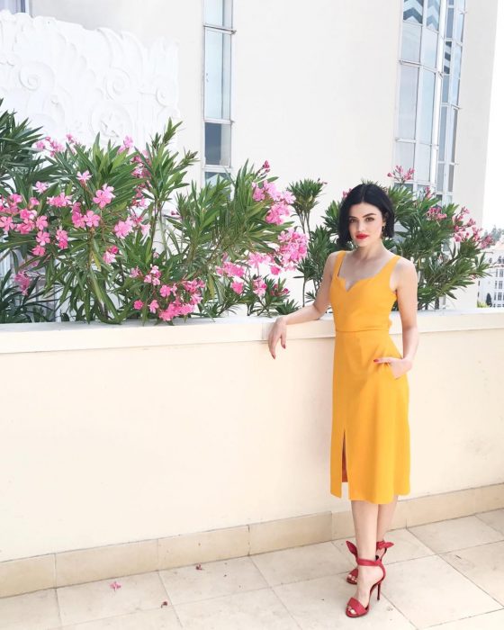 Lucy Hale usando un vestido de color amarillo y zapatos rojos 