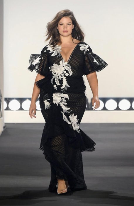 Modelo Tara Lynn caminando por la paserla con un vestido largo de color negro con estampado en color blanco