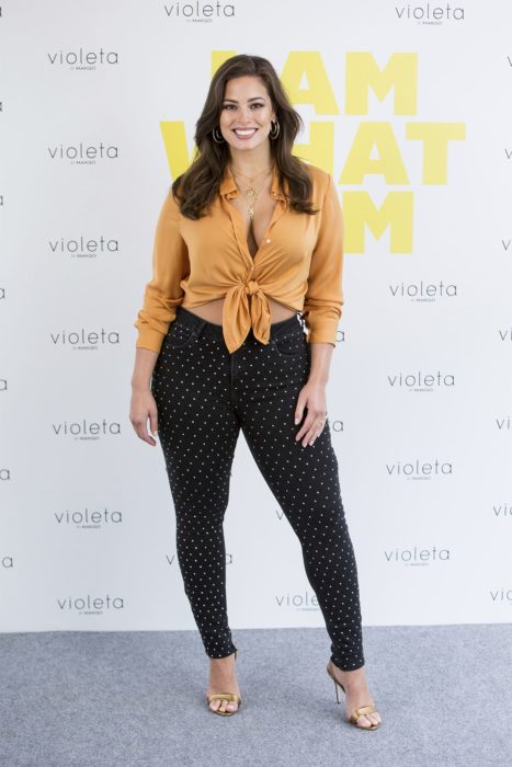 Ashley Graham posando para una alfombra roja con un pantalón negro, blusa de manga larga y cuello 