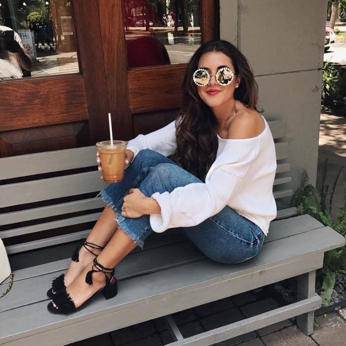 Chica sentada en una banca tomando café y mostrando sus zapatos de tacón