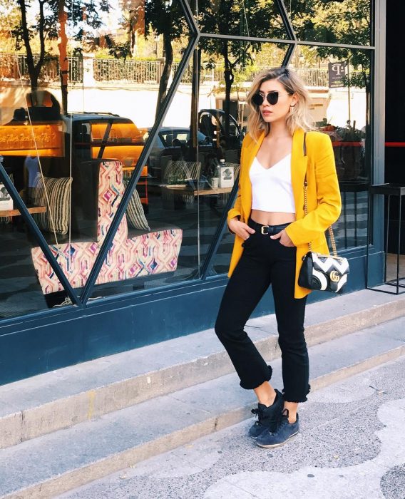 mujer con pantalón negro bralete blanco y saco amarillo 