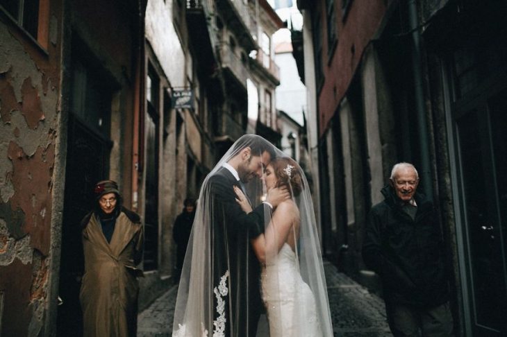 Pareja de novios en un callejón besándose durante una sesión de fotos el día de su boda 