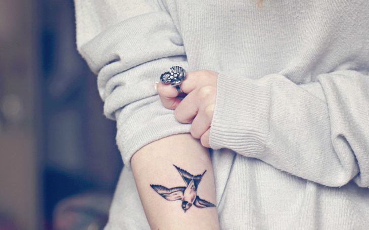 Chica mostrando su tatuaje de una ave en el brazo