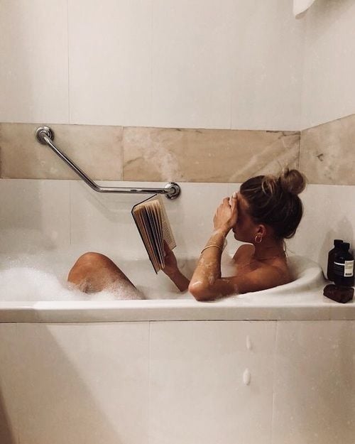 Chica tomando una ducha en una tina mientras lee