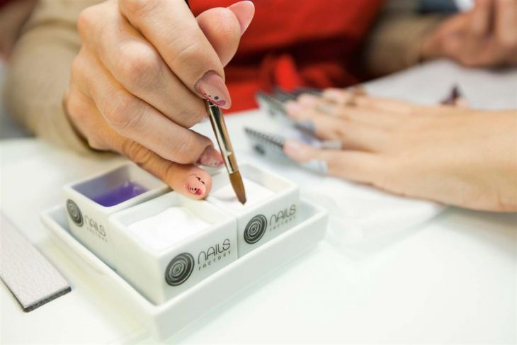 Chica aplicando acrilico en las uñas de otra mujer