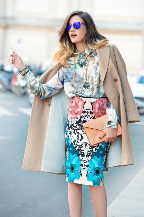 Chica parando un taxi usando un saco de color beige, falda de estampado floral y blusa con estampado de color gris 